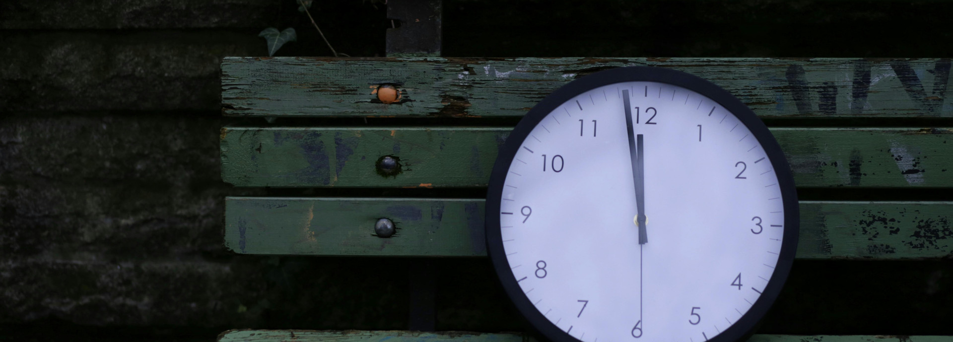 Eine Uhr, die zwölf Uhr anzeigt, liegt auf einer Parkbank.